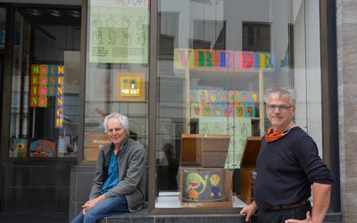 Gerhard Fauser und Uli Lüttringhaus  (von links) von der „Schule in der Werkstatt“ des Frère-Roger-Kinderzentrums präsentieren die Friedensprojekte junger Schulverweigerer in der Augsburger Innenstadt (Foto: KJF/Ronja Mößbauer).